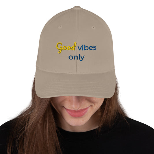 White baseball cap featuring embroidered text reading ‘GOOD VIBES ONLY’ in yellow, placed beside black headphones and stationery—modern, stylish, and perfect for casual wear.