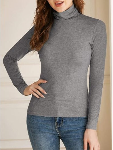 Woman wearing an gray turtleneck long-sleeve top paired with blue jeans, standing in front of decorative wall panels—sleek, stylish, and perfect for layering.