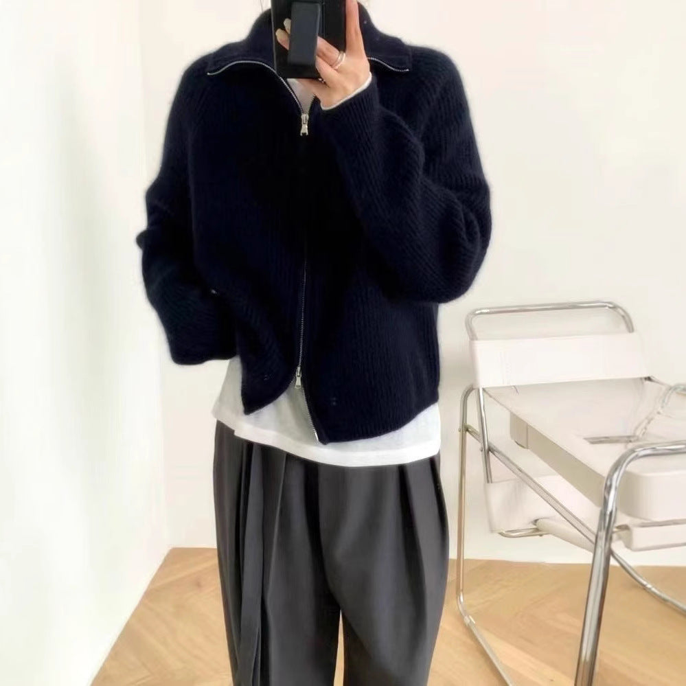 Woman wearing a navy ribbed knit sweater with a high collar and a partially zipped front, styled with light pink pants and delicate accessories—cozy, stylish, and perfect for layering.