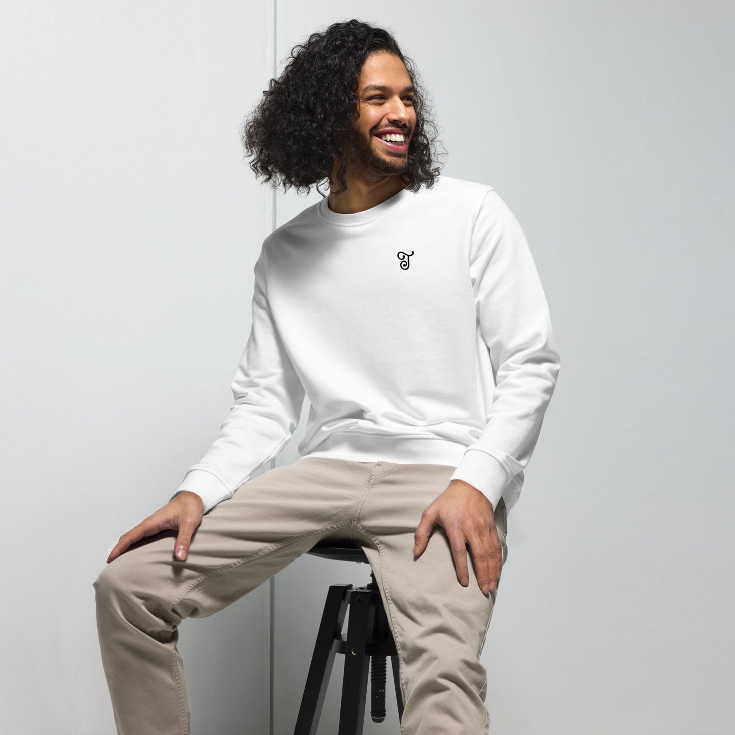 White sweatshirt featuring an embroidered letter ‘T’ on the left chest, worn with beige pants, seated on a black stool against a white background—modern, stylish, and available in multiple colors.