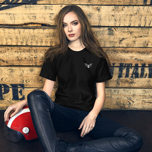 Black women’s t-shirt featuring a small white geometric bat logo on the left side of the chest, worn while seated on a wooden floor with a red and white helmet nearby—sleek, minimalist, and perfect for casual and athletic wear.