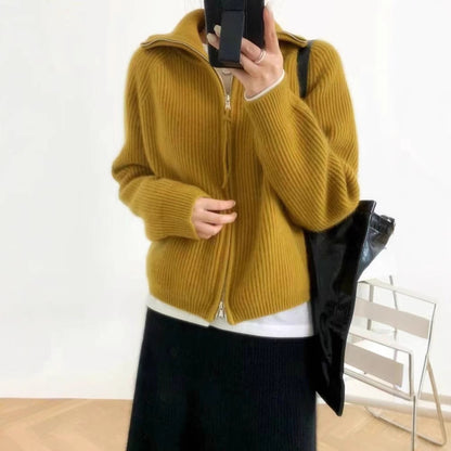 Woman wearing a yellow mustard ribbed knit sweater with a high collar and a partially zipped front, styled with light pink pants and delicate accessories—cozy, stylish, and perfect for layering.